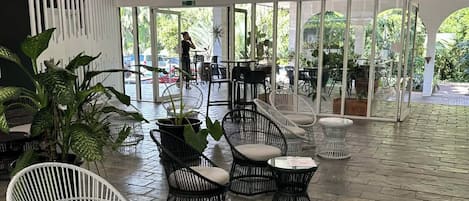 Un espacio interior amplio con mobiliario de mimbre, ventilador de techo y ventanas grandes.