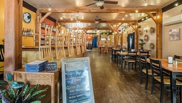 L’intérieur d’un restaurant avec des poutres en bois, des tables, des chaises et un menu écrit sur un tableau noir.