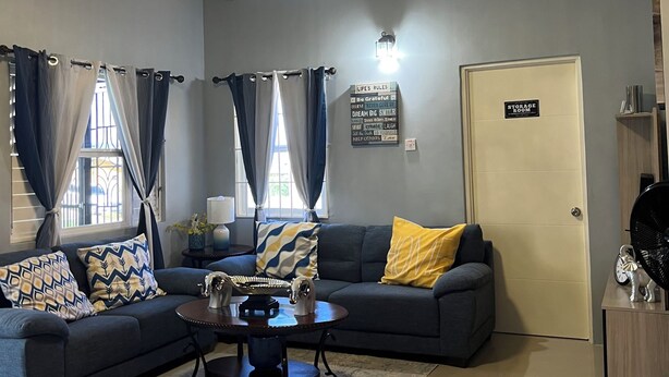 A living room with a sectional sofa, a coffee table, a chandelier, and a door labeled 'STORAGE ROOM'. - Cozy 2-bedroom house in peaceful Florence Hall Village with AC (Florence Hall Village)