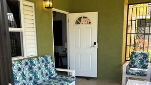 A covered patio area with a white door, a sofa, and a chair with floral upholstery. - Cozy 2-bedroom house in peaceful Florence Hall Village with AC (Florence Hall Village)