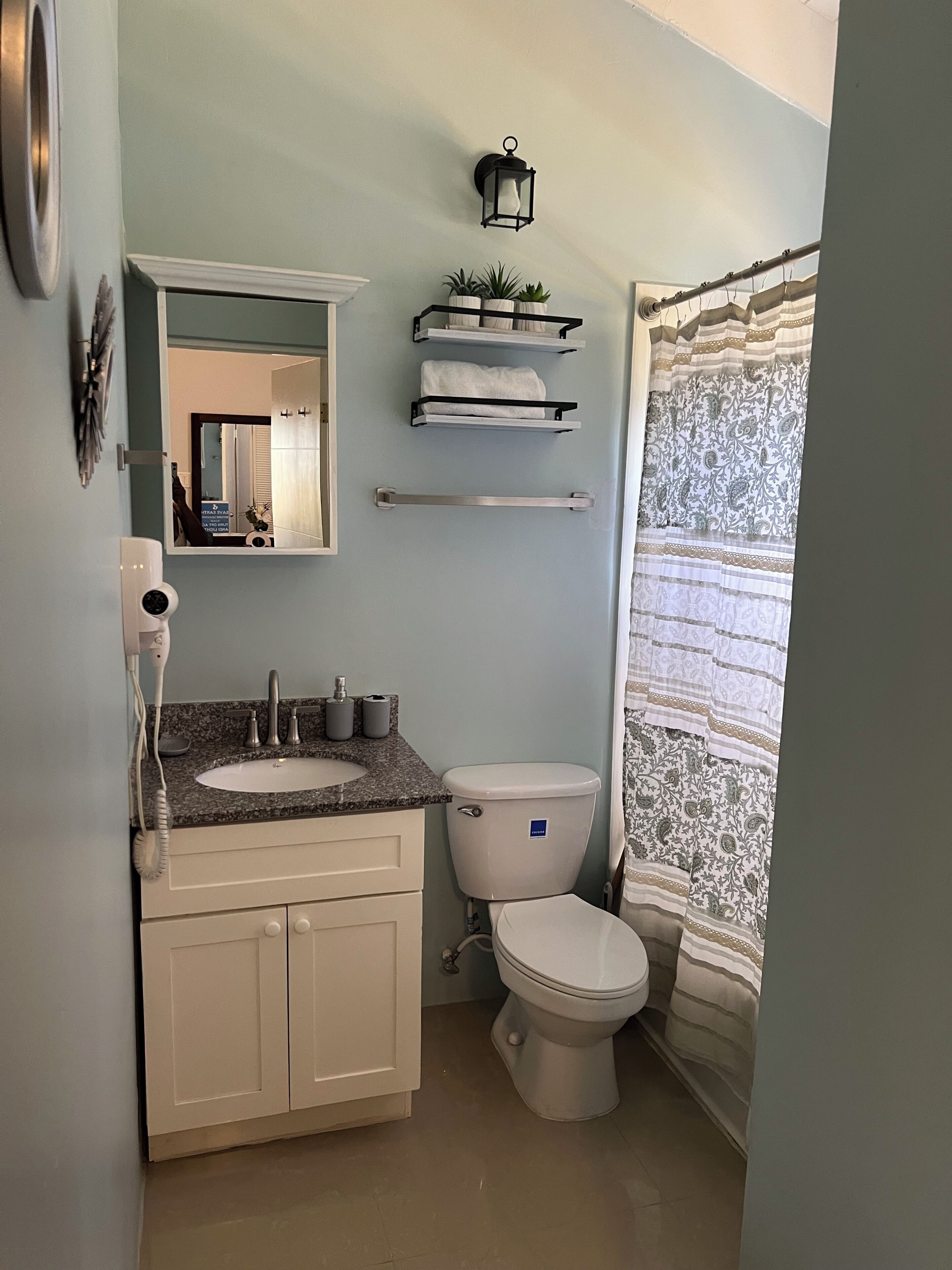 A bathroom with a sink, toilet, and a mirror. There is a towel rack above the toilet and a wall-mounted light fixture.
