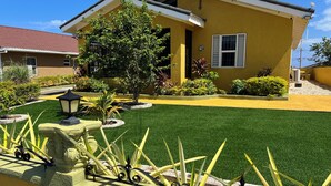 A yellow building with a green lawn, a tree, and a decorative fence. - Cozy 2-bedroom house in peaceful Florence Hall Village with AC (Florence Hall Village)