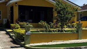 A yellow building with a large window, a number sign '298', and a paved driveway. - Cozy 2-bedroom house in peaceful Florence Hall Village with AC (Florence Hall Village)