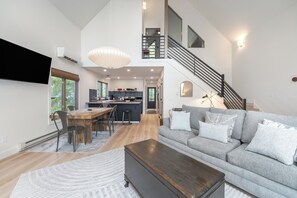 Ein großzügiger Wohnbereich mit Sofa, Couchtisch und Esstisch. Eine Treppe führt in einen oberen Bereich.