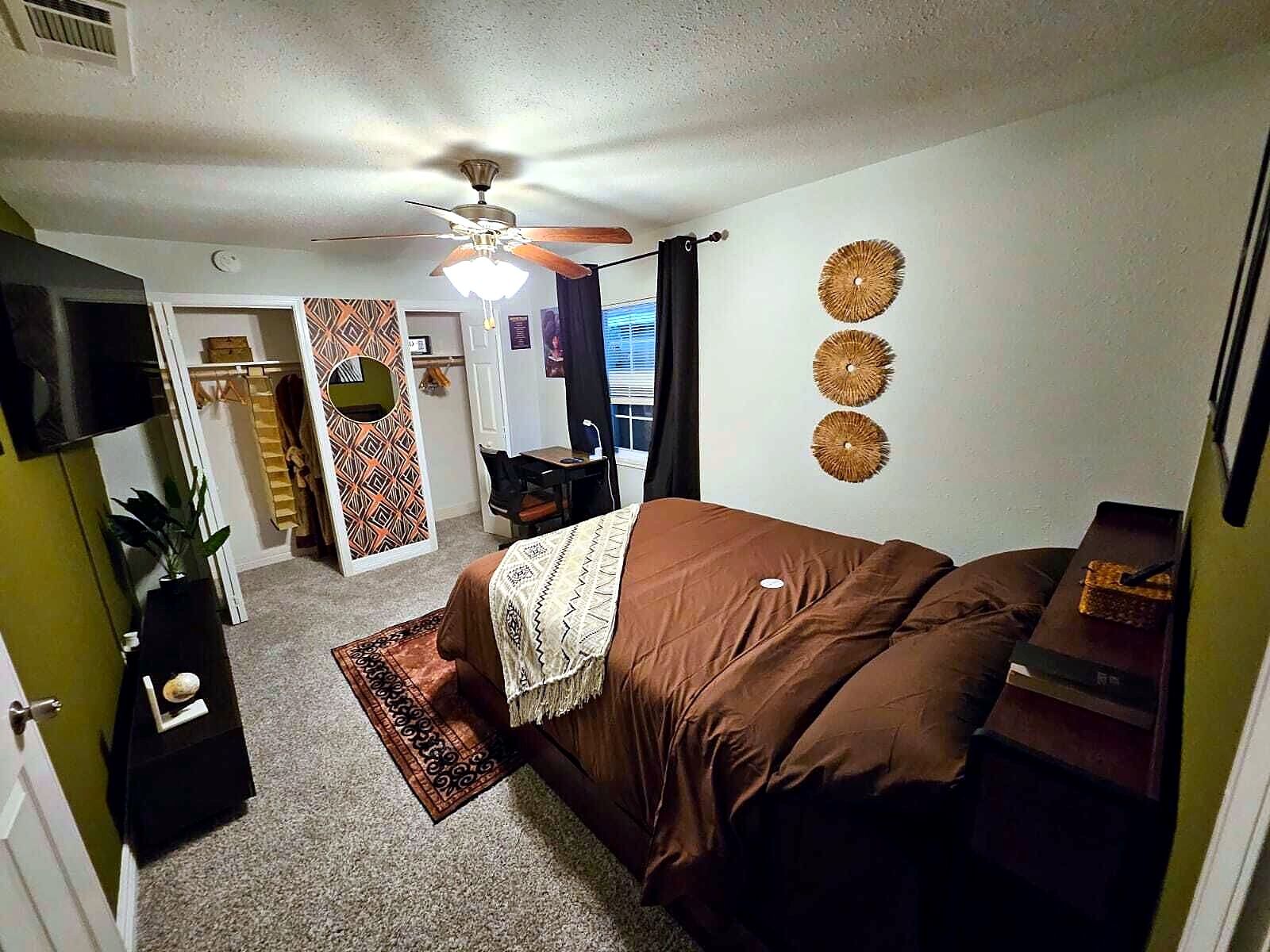 A bedroom with a bed, a ceiling fan, a desk, and a chair.