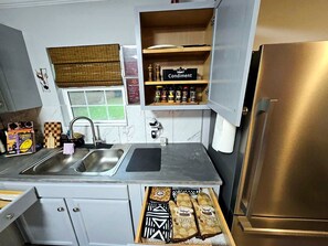 A kitchen with a stainless steel sink, a window with blinds, a countertop with condiments, and a drawer with packaged goods. - Spacious 3BR w/ Hot Tub, Grill & Game Room Near NRG, Med Ctr, Downtown & Hobby (Houston)