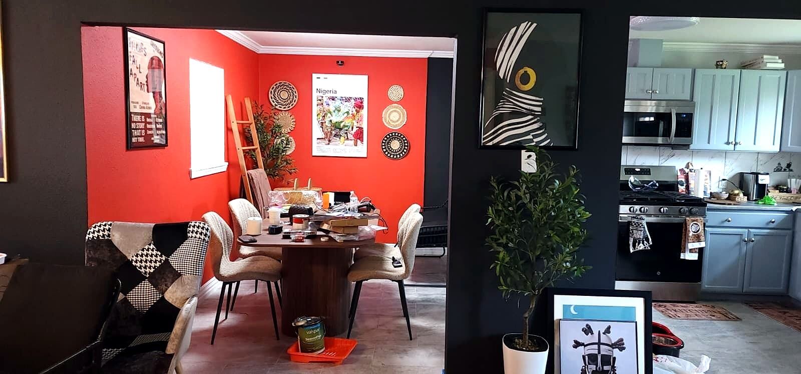 A dining area with a red wall, a table with chairs, and a potted plant.