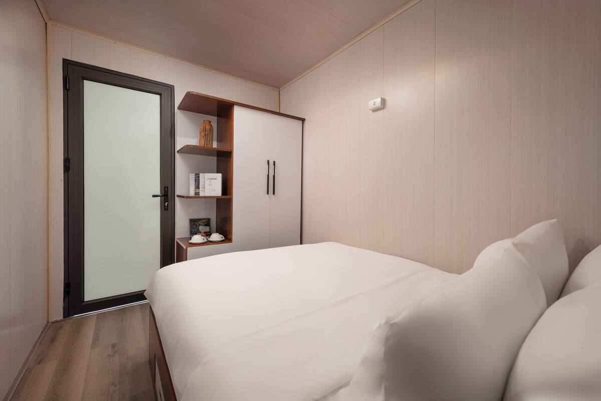 A bedroom with a bed, a wardrobe, and a shelf with items.