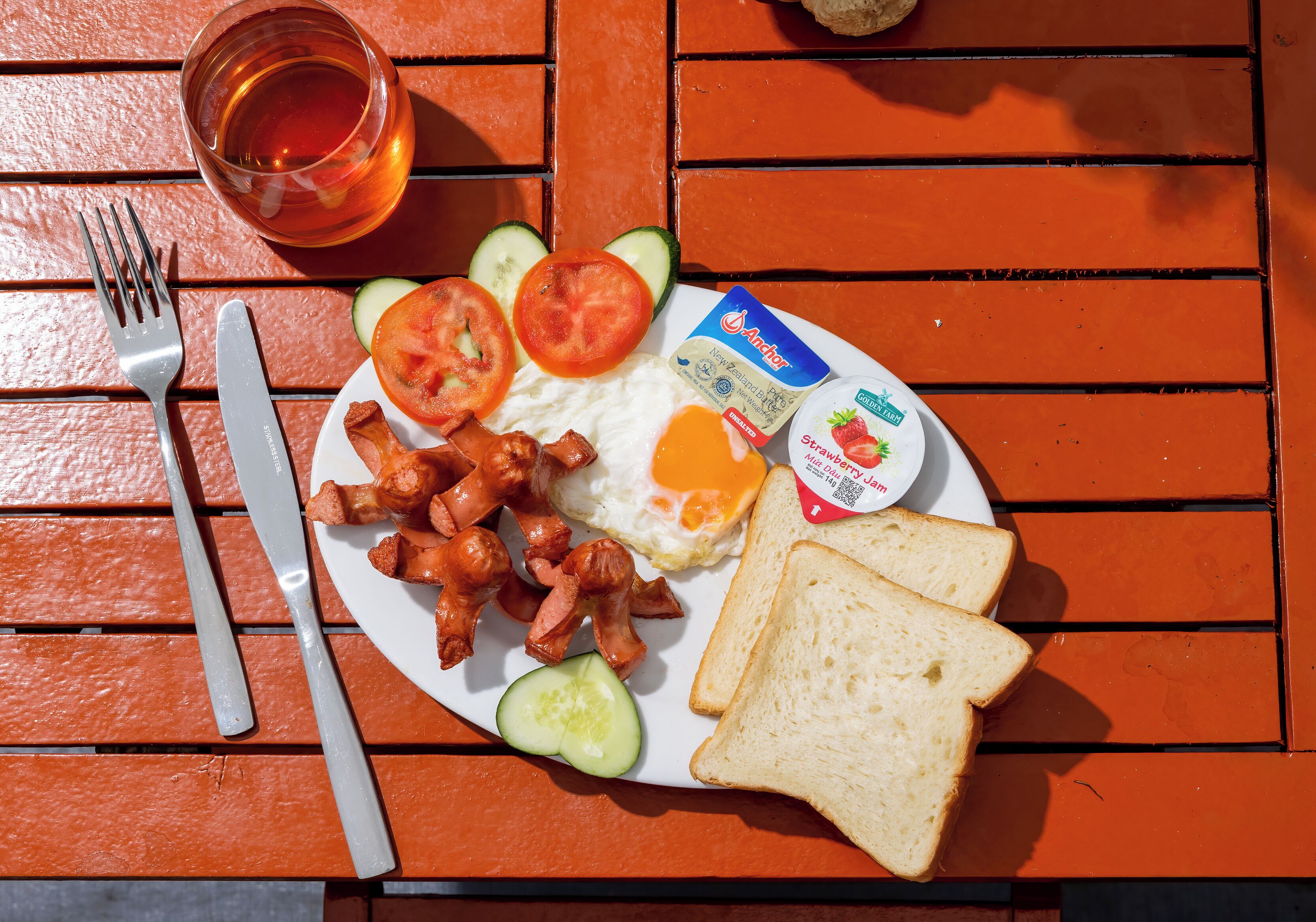 A plate with eggs, bacon, toast, and a glass of tea on a wooden table.