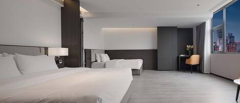 A hotel room with a large bed, a desk, and a chair, with a city view through the window.