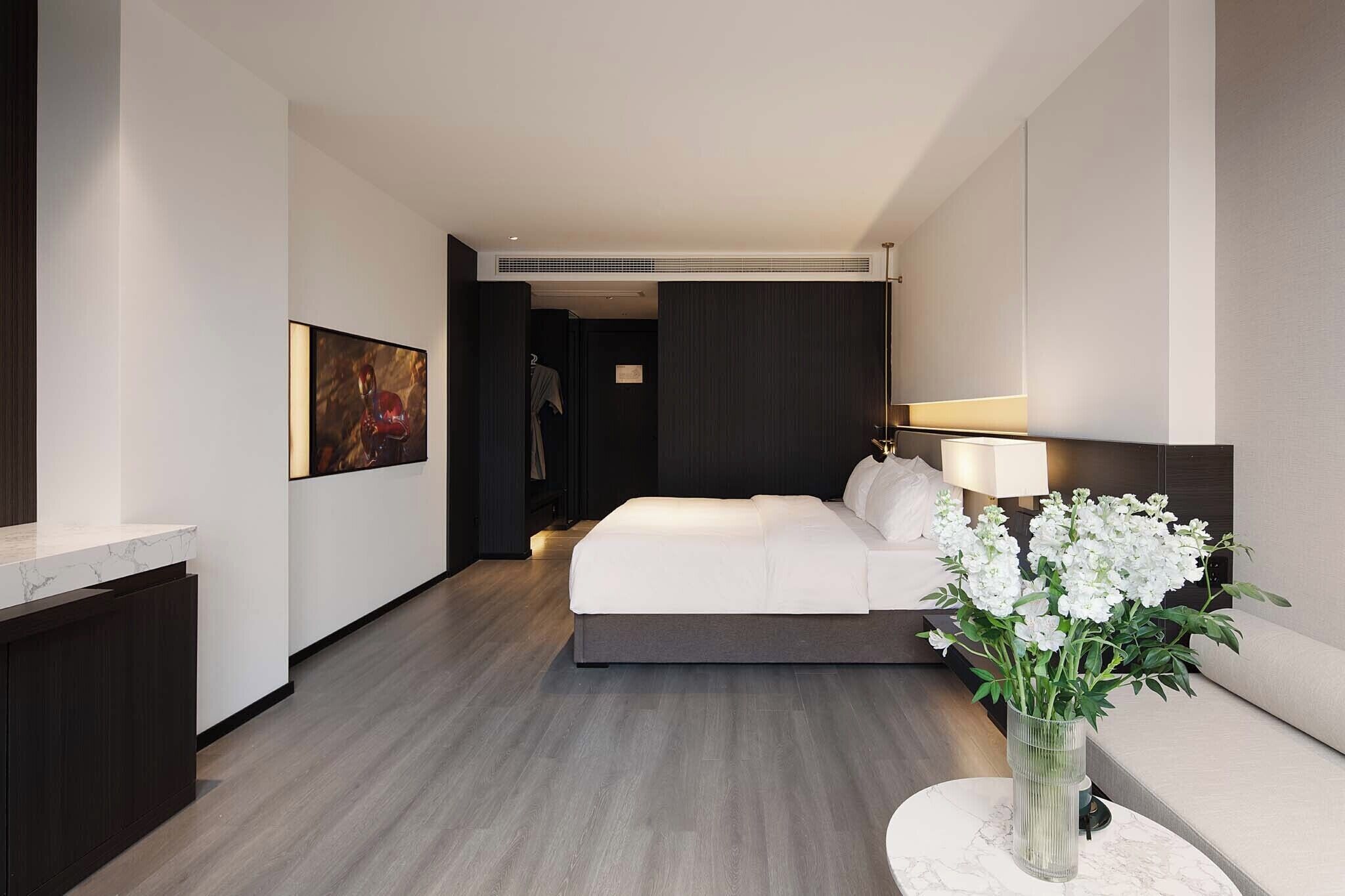 A modern hotel room with a large bed, a bedside table, a vase of flowers, and a painting on the wall.