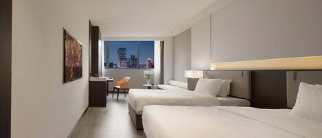A hotel room with two beds, a desk, a chair, and a large window with a city view.