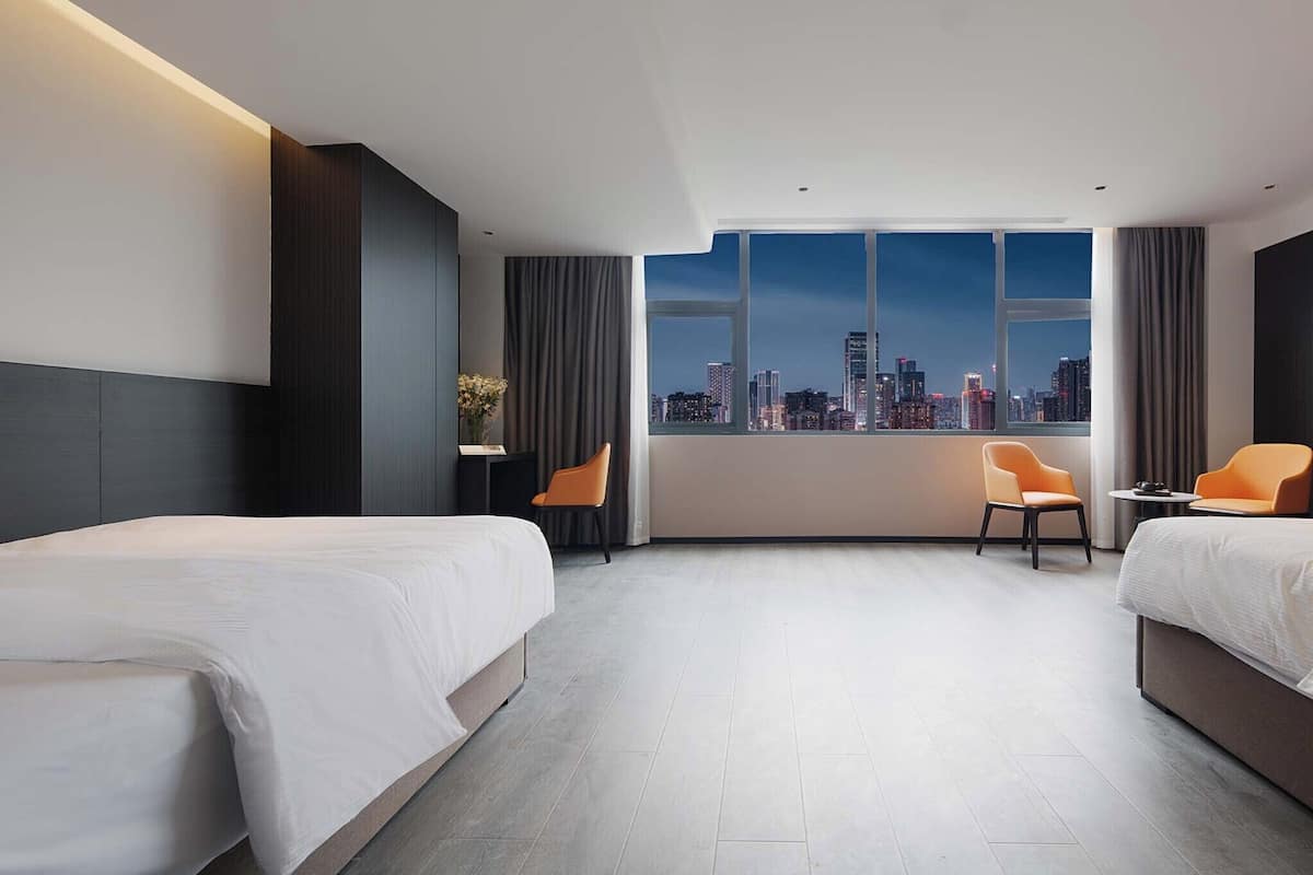 A hotel room with two beds, a city view, a small table, and two chairs.