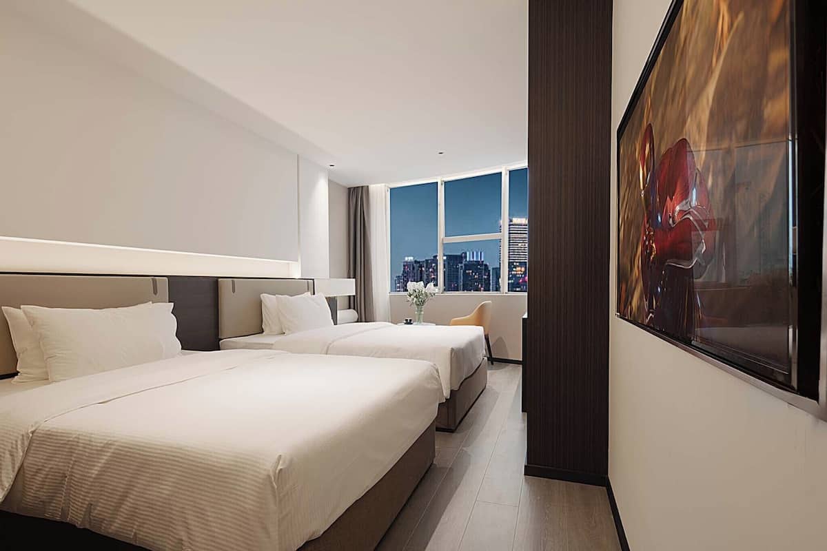 A hotel room with two beds, a large window with a city view, and a painting on the wall.