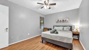 Una camera da letto con un letto, un ventilatore a soffitto, una finestra, un comodino e un quadro appeso al muro.