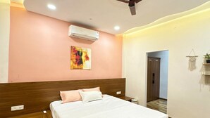 A bedroom with a bed, an air conditioner, a ceiling fan, a wall-mounted artwork, and a wooden headboard. - Escape & Relax at Kaash Villa, 2BR Luxury Stay in Indore, Projector,Outdoor Area (Indore)