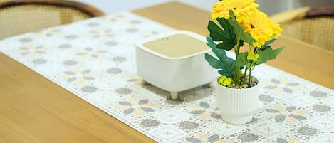 A wooden table with a lace tablecloth, a white ceramic pot with yellow flowers, and a white ceramic object.
