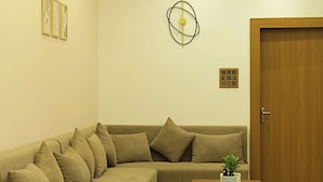 A living room with a sectional sofa, a wooden door, a ceiling fan, recessed lighting, and a wall-mounted abstract art piece. - Escape & Relax at Kaash Villa, 2BR Luxury Stay in Indore, Projector,Outdoor Area (Indore)