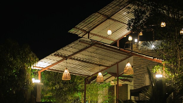 A covered outdoor area with hanging lights, a wooden fence, and a pathway leading to a building. - Escape & Relax at Kaash Villa, 2BR Luxury Stay in Indore, Projector,Outdoor Area (Indore)