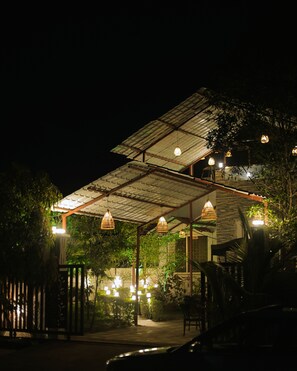 Un espace extérieur abrité, agrémenté de guirlandes lumineuses, d’une clôture en bois et d’un chemin menant à un bâtiment.