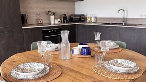 Une cuisine moderne avec des meubles de couleur sombre, une table ronde en bois dressée pour le repas et un évier bien visible.