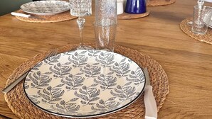 Une table à manger dressée avec des assiettes à motifs, de la verrerie transparente et un vase décoratif.
