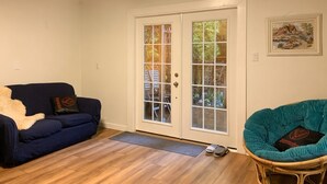 A living room with a blue sofa, a teal chair, a white door with glass panels, and a framed picture on the wall. - Sweet One Bedroom (Victoria)