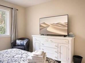 A bedroom with a bed, a chair, a dresser, a television, and a window with curtains. - Sweet One Bedroom (Victoria)