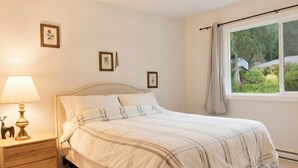 A bedroom with a bed, bedside table, lamp, and framed pictures on the wall. - Sweet One Bedroom (Victoria)