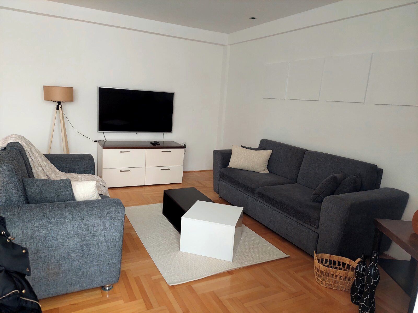 A living room with a grey sofa, a white coffee table, a flat-screen TV, a lamp, and a wooden floor.