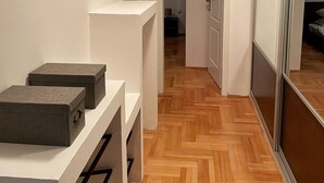 Ein Korridor mit Holzdielen im Fischgrätmuster, weißen Wänden und einer Schiebetür aus Glas auf der rechten Seite.