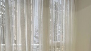 Ein Esstisch mit vier gewebten Tischsets, umgeben von Stühlen, in einem Raum mit transparenten Vorhängen und Blick auf Gebäude.