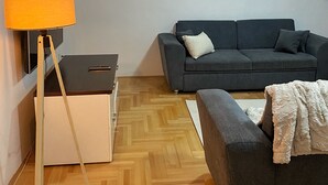 Ein Wohnzimmer mit grauem Sofa, einer Lampe, einem weißen Schrank und einem Holzboden mit Fischgrätmuster.