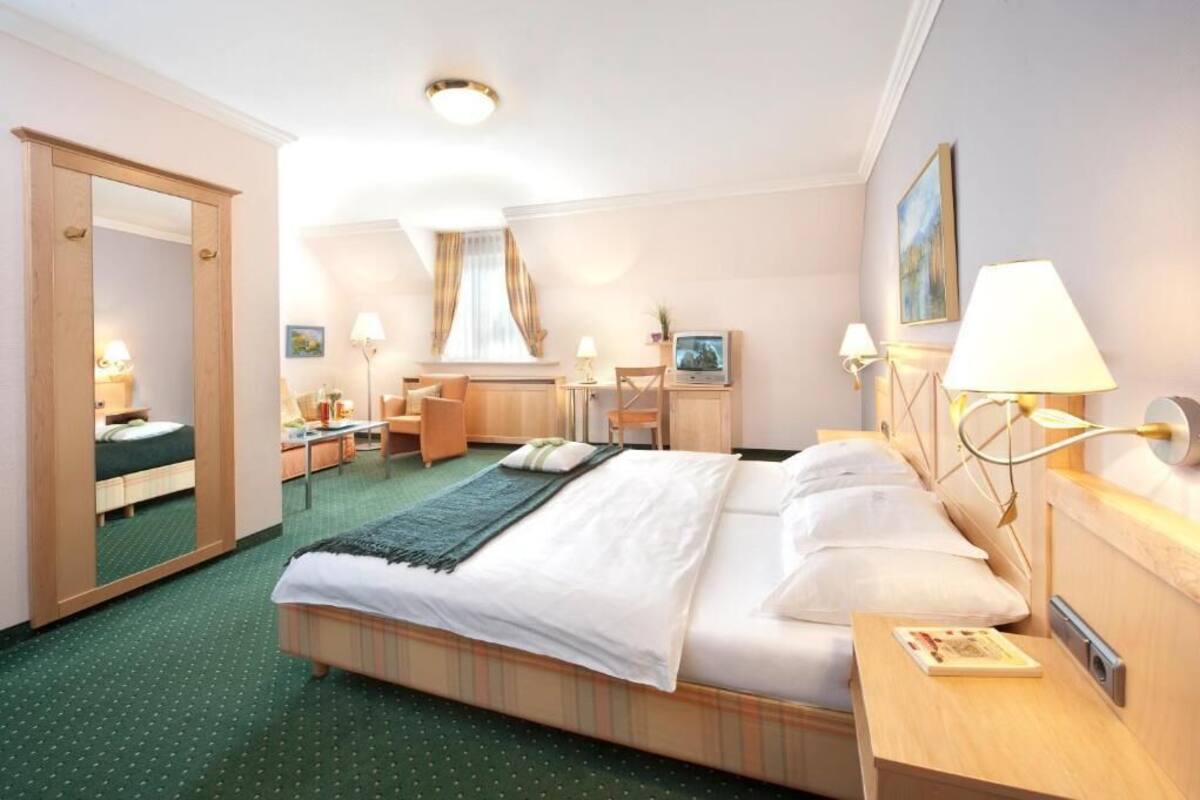 A hotel room with a bed, bedside table, lamp, and a desk with a chair.