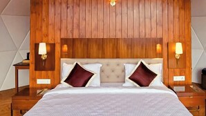 A bedroom with a wooden panel headboard, two bedside lamps, a bed with white bedding and maroon pillows, and a wooden nightstand on each side.