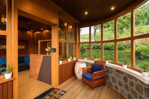 A wooden interior with a reception desk, seating area, and large windows overlooking greenery. - LushGreen Kodai by Arcadia (Kodaikanal)