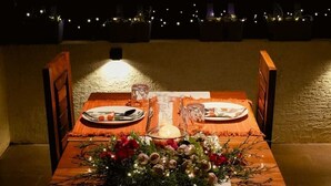 A dining table set for two with a candle centerpiece, a floral arrangement, and a view of the night sky.