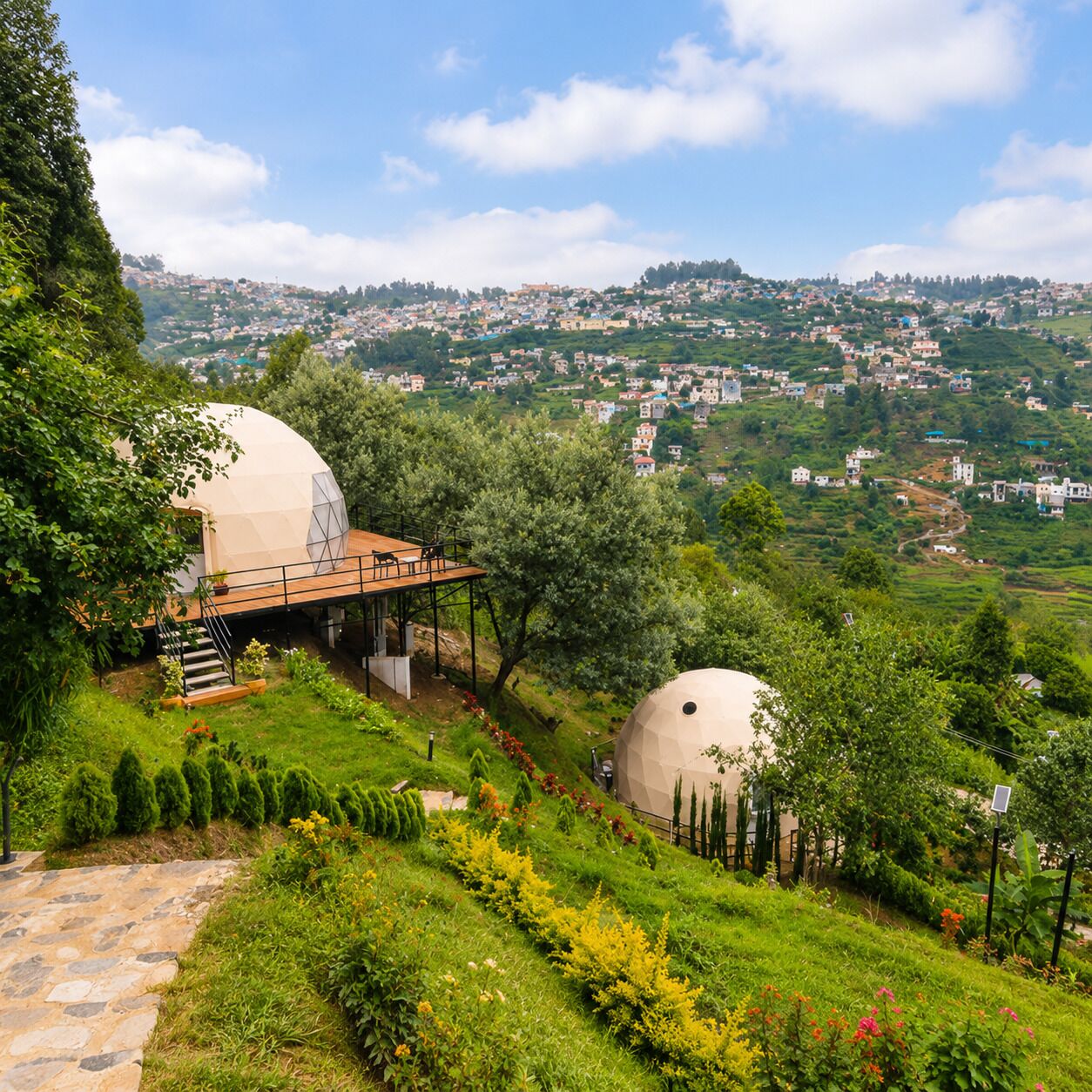 A hillside property with two large dome-shaped structures, a stone pathway, and a view of a town in the distance.