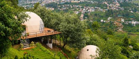A hillside property with two large dome-shaped structures, a stone pathway, and a view of a town in the distance.
