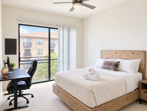 A hotel room with a bed, a desk with a computer, a chair, and a ceiling fan. - 2BR Traveler / Domain Louis Vuitton Building (Austin)