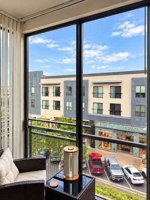 A modern hotel room with a large window offering a view of a city street and a building with a 'GUCCI' sign. - 2BR Traveler / Domain Louis Vuitton Building (Austin)