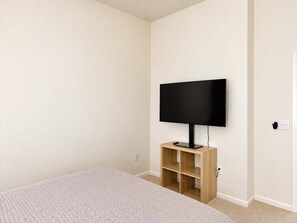 A bedroom with a bed, a television on a stand, and a door. - 2BR Traveler / Domain Louis Vuitton Building (Austin)