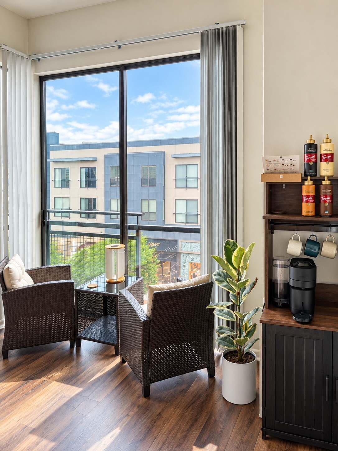 Un salon moderne avec une grande fenêtre, des meubles en osier, une plante en pot et une machine à café.