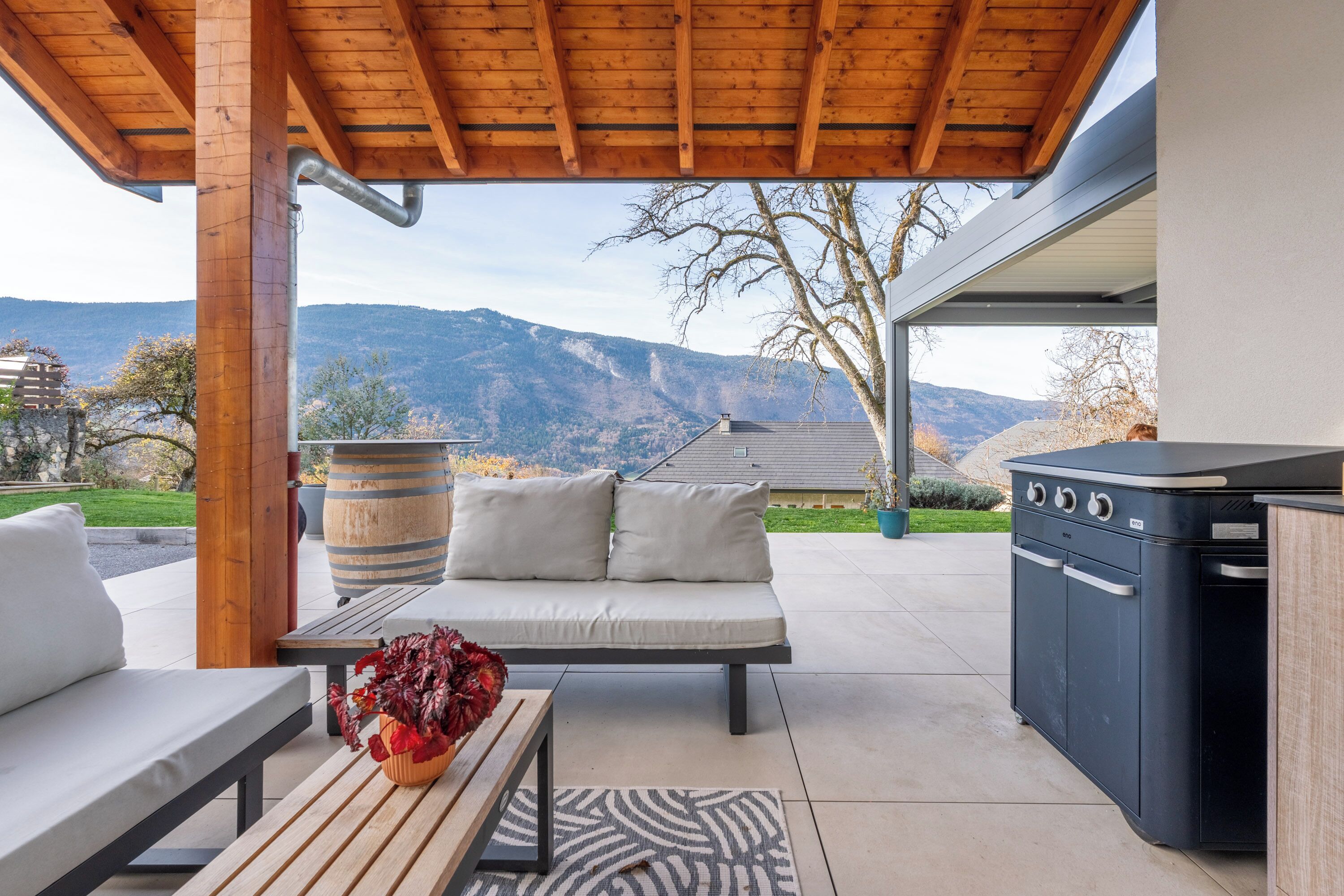 Une terrasse extérieure avec un banc en bois, un canapé, un barbecue et une vue sur les montagnes.