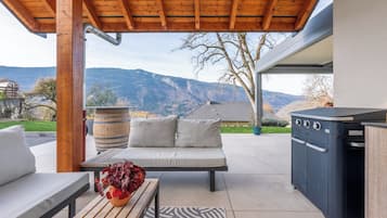 An outdoor patio with a wooden bench, a sofa, a grill, and a view of mountains.