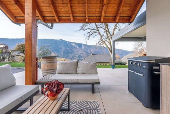 An outdoor patio with a wooden bench, a sofa, a grill, and a view of mountains.