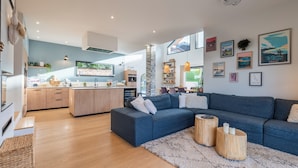 Uma sala de estar moderna com um sofá azul, mesa de centro de madeira e cozinha ao fundo.