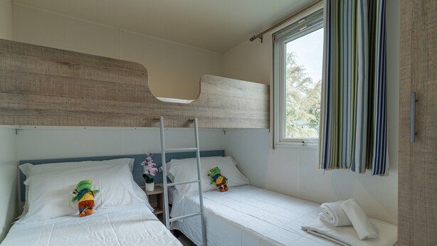 A room with bunk beds, a ladder, a window with curtains, and a small table with a flower. - Vigna Sul Mar Family Collection (Comacchio)