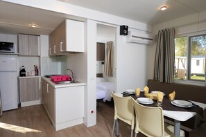 Une petite cuisine équipée d’un four à micro-ondes, d’un grille-pain et d’un évier. Un coin repas est aménagé avec une table, des chaises et une fenêtre avec des rideaux.