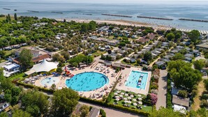 An aerial view of a coastal resort with multiple swimming pools, beach access, and a marina. - Vigna Sul Mar Family Collection (Comacchio)